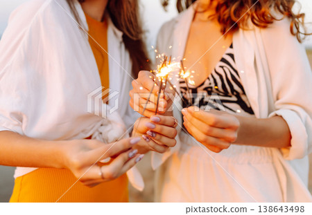 The sparklers in the hands of young women on the beach. Happy women walking with sparkler fireworks The sparklers in the hands of young women on the beach. Happy women walking with sparkler fireworks 138643498