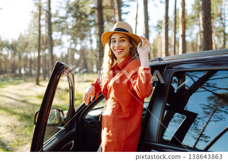 Young woman enjoying a sunny day by her car in forest setting during the afternoon. Summer trip Young woman enjoying a sunny day by her car in forest setting during the afternoon. Summer trip 138643863