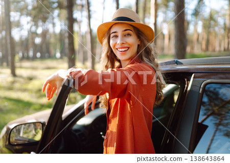 Young woman enjoying a sunny day by her car in forest setting during the afternoon. Summer trip Young woman enjoying a sunny day by her car in forest setting during the afternoon. Summer trip 138643864