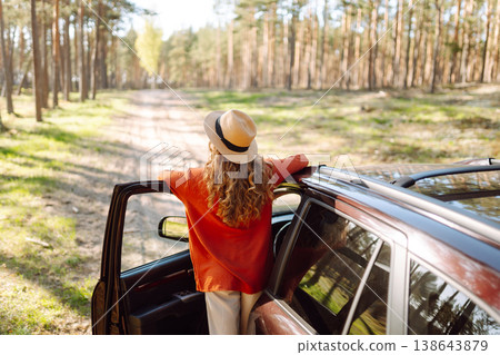 Young woman enjoying a sunny day by her car in forest setting during the afternoon. Summer trip Young woman enjoying a sunny day by her car in forest setting during the afternoon. Summer trip 138643879