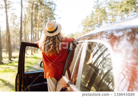 Young woman enjoying a sunny day by her car in forest setting during the afternoon. Summer trip Young woman enjoying a sunny day by her car in forest setting during the afternoon. Summer trip 138643880
