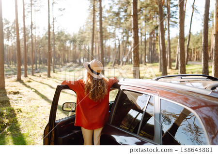 Young woman enjoying a sunny day by her car in forest setting during the afternoon. Summer trip Young woman enjoying a sunny day by her car in forest setting during the afternoon. Summer trip 138643881