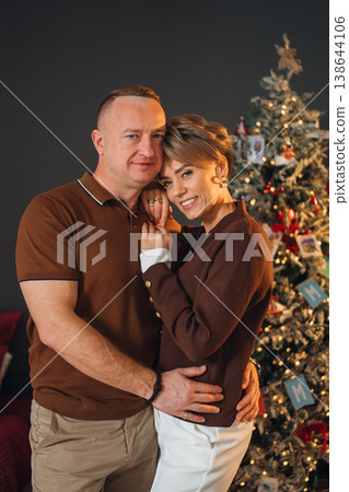 Couple poses together by the Christmas tree in a cozy setting Couple poses together by the Christmas tree in a cozy setting 138644106