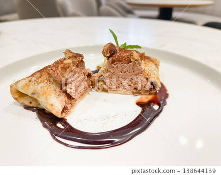 A crepe wrapped around chocolate whipped cream. Topped with chocolate sauce. Cross-section. A crepe wrapped around chocolate whipped cream. Topped with chocolate sauce. Cross-section. 138644139