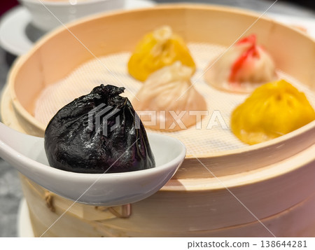 Steamed dishes. Colorful, flavored xiao long bao (soup dumplings). Close-up of a black xiao long bao. 138644281