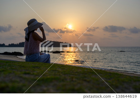 A Japanese woman wearing a hat gazes at the sea at sunset. A Japanese woman wearing a hat gazes at the sea at sunset. 138644619