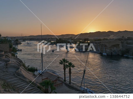 夕陽西下,尼羅河寧靜祥和,阿斯旺的岩石河岸,遠處漂浮著一艘三角帆船。 夕陽西下,尼羅河寧靜祥和,阿斯旺的岩石河岸,遠處漂浮著一艘三角帆船。 138644752