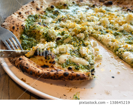 They are cutting the pizza to serve it. It's topped with pesto, boiled eggs, and cheese. They are cutting the pizza to serve it. It's topped with pesto, boiled eggs, and cheese. 138645219