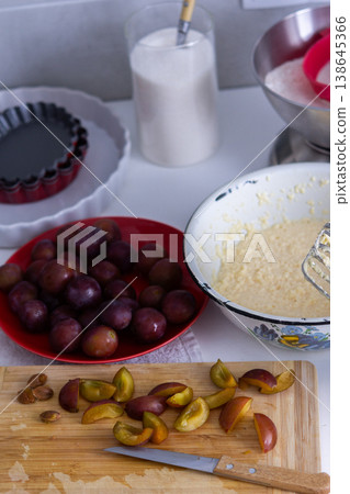 Cook is preparing to make plum pie in a home kitchen. Ingredients like plums, flour, sugar, and butter are on the counter. Tools for mixing and baking are nearby Cook is preparing to make plum pie in a home kitchen. Ingredients like plums, flour, sugar, and butter are on the counter. Tools for mixing and baking are nearby 138645366
