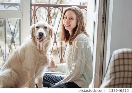 Woman and golden retriever smiling by balcony window Woman and golden retriever smiling by balcony window 138646213