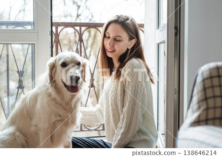 Woman petting golden retriever dog in front of a balcony door 138646214
