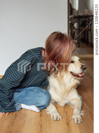 Girl embracing golden retriever dog on wooden floor Girl embracing golden retriever dog on wooden floor 138646220