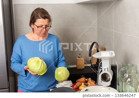 A woman is in a kitchen working on fermenting cabbage. She is holding a cabbage and preparing it for the fermentation process. It is daylight in the kitchen A woman is in a kitchen working on fermenting cabbage. She is holding a cabbage and preparing it for the fermentation process. It is daylight in the kitchen 138646247