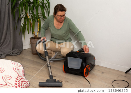Person is getting a vacuum cleaner ready for use in a living room. The vacuum is plugged in and they are holding the hose, preparing to clean the floor Person is getting a vacuum cleaner ready for use in a living room. The vacuum is plugged in and they are holding the hose, preparing to clean the floor 138646255