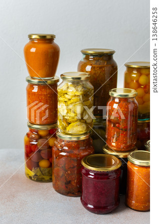 Canned vegetables and fruits are stacked on a shelf, prepared for winter use. Various jars hold different preserves, showcasing careful efforts for storing food during the season 138646258