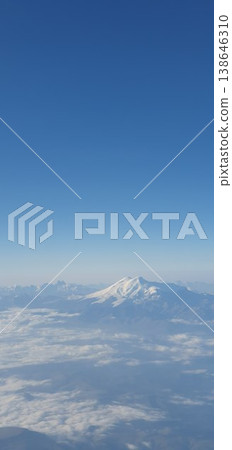 Phone photo of snow-covered Mount Elbrus peeking through clouds, viewed from an airplane window. Aerial mountain scene showing dramatic altitude, winter landscape, and travel perspective. Phone photo of snow-covered Mount Elbrus peeking through clouds, viewed from an airplane window. Aerial mountain scene showing dramatic altitude, winter landscape, and travel perspective. 138646310