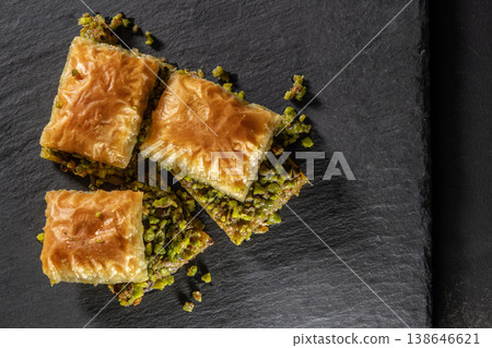 Traditional pistachio baklava on granite. Close-up of pistachio baklava on granite background. Turkish dessert baklava with pistachios. Pistachio baklava on stone surface. Traditional pistachio baklava on granite. Close-up of pistachio baklava on granite background. Turkish dessert baklava with pistachios. Pistachio baklava on stone surface. 138646621
