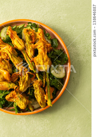 Roasted zucchini flowers are placed on a bed of fresh greens, cucumbers, and broccoli during a summer meal. This dish highlights the flavors of summer ingredients 138646887