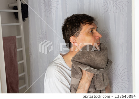 A 53-year-old man stands in a bathroom. He is drying his face with a towel after washing it. The man appears focused as he prepares for the day ahead A 53-year-old man stands in a bathroom. He is drying his face with a towel after washing it. The man appears focused as he prepares for the day ahead 138646894