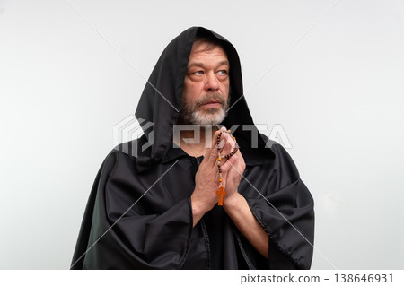 Elderly monk in black robe praying with rosary on white background. 138646931
