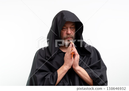 Elderly monk in black robe praying with rosary and cross, isolated. Elderly monk in black robe praying with rosary and cross, isolated. 138646932