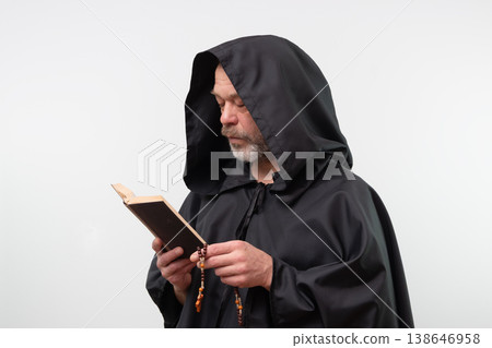 Bearded monk with hood reading religious book on white background. 138646958