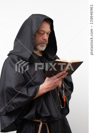 Male monk reading book holding rosary wearing black robe. 138646961