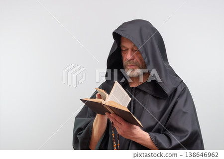 Male monk attentively reading book wearing black robe, isolated. 138646962