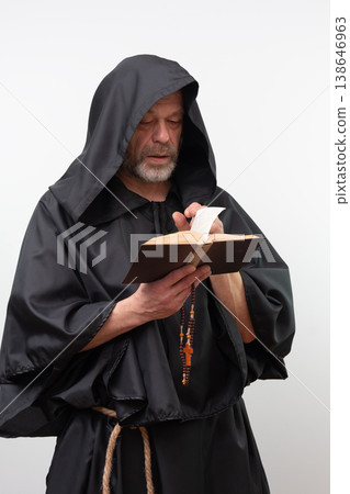 Male monk reading book holding rosary wearing black robe. 138646963