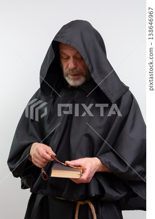 Bearded monk in hood looking down holding rosary and book. Bearded monk in hood looking down holding rosary and book. 138646967