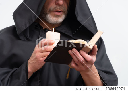 Male monk reading book with candle wearing black robe. 138646974