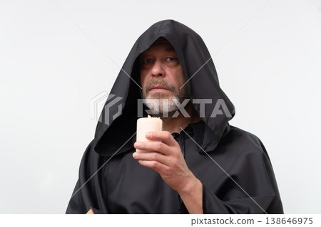 Bearded monk in hood looking forward holding candle and book. 138646975