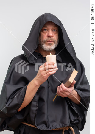 Bearded monk in hood looking at camera by candle light. 138646976