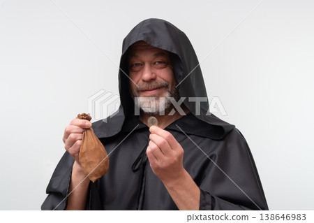 Elderly bearded monk smiling while holding coin isolated on white background. Elderly bearded monk smiling while holding coin isolated on white background. 138646983