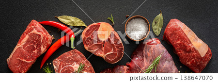 Various cuts of beef steak are shown with herbs, spices, and oil on a dark surface. Perfect for those looking to prepare or grill different beef dishes at home, banner 138647070