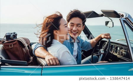 Happy Asian couple laughing together in vintage blue convertible car during romantic seaside road trip vacation with camera and luggage 138647414