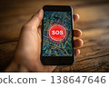 A hand holding a smartphone displaying an SOS message on the screen. 138647646