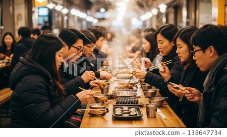Food - Korean People Eating Traditional Street Food at Crowded Indoor Market Stall with Chopsticks and Steam 138647734