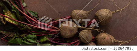 Beets with green leaves rest on a brown surface in a kitchen. The setting is warm and hints at fresh produce ready for cooking or eating, banner Beets with green leaves rest on a brown surface in a kitchen. The setting is warm and hints at fresh produce ready for cooking or eating, banner 138647983
