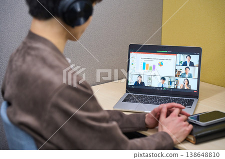 The back view of a businessman wearing headphones and participating in an online meeting in a private office booth. The back view of a businessman wearing headphones and participating in an online meeting in a private office booth. 138648810