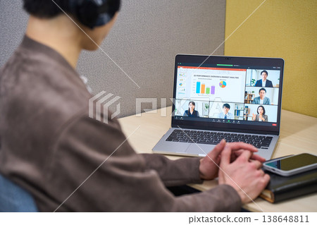 The back view of a businessman wearing headphones and participating in an online meeting in a private office booth. The back view of a businessman wearing headphones and participating in an online meeting in a private office booth. 138648811