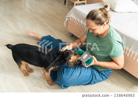 Woman sitting on floor, petting and interacting with her domestic dog holding a toy, showing a strong companionship bond Woman sitting on floor, petting and interacting with her domestic dog holding a toy, showing a strong companionship bond 138648983