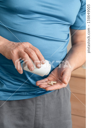Man holding a white bottle, pouring two capsules onto his open palm, symbolizing health and wellness. Taking care of your health and disease prevention Man holding a white bottle, pouring two capsules onto his open palm, symbolizing health and wellness. Taking care of your health and disease prevention 138649005