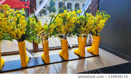Creative display of yellow rubber boots filled with colorful flowers in a sunny interior Creative display of yellow rubber boots filled with colorful flowers in a sunny interior 138649116