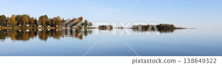 Golden and red colored autumn trees in Vita Sannar mirroring in Lake Vanern, Sweden. 138649322