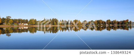 Multi colored autumn trees in Vita Sannar mirroring in Lake Vanern, Sweden. 138649324