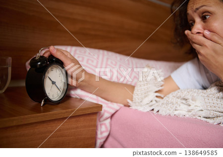 Close-up Shocked Woman Reaching Alarm Clock in Bed After Oversleeping 138649585