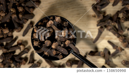 Cloves in black scoop on wooden surface with scattered cloves around it Cloves in black scoop on wooden surface with scattered cloves around it 138650998