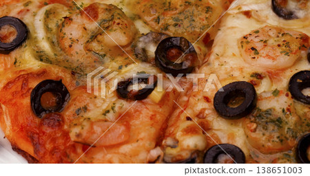 Delicious pizza slices topped with shrimp and olives on a white plate in a casual dining setting 138651003