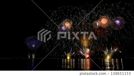 Colorful fireworks light up the night sky over water during a celebration near a city in summer Colorful fireworks light up the night sky over water during a celebration near a city in summer 138651153